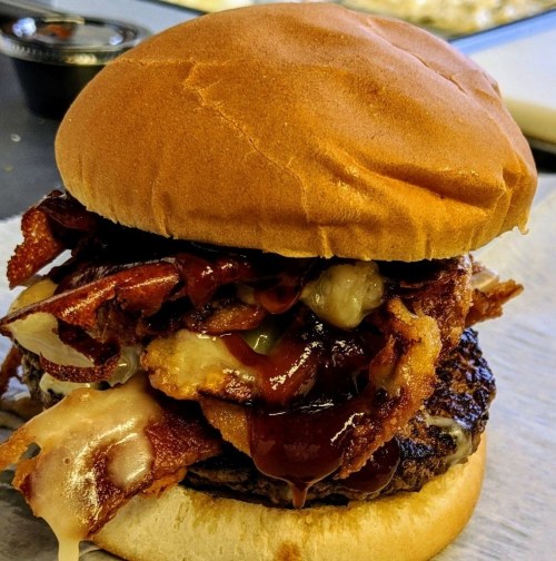 A close-up of a juicy burger topped with bacon, barbecue sauce, and melted cheese, served on a soft bun.