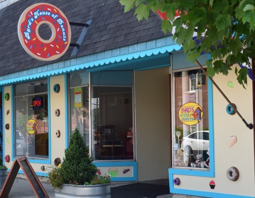 A colorful donut shop with a sign reading "Burd's House of Donuts" and large windows displaying treats.