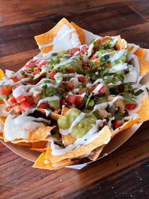 A colorful plate of nachos topped with guacamole, pico de gallo, and drizzled with sour cream on a wooden table.