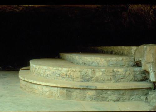 Stone steps leading into a dark cave, with a smooth, curved design and a natural rock backdrop.