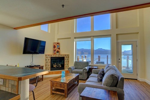 Bright living room with large windows, a fireplace, and a view of mountains and water. Cozy furniture and a TV present.