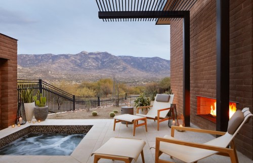 A serene outdoor patio with lounge chairs, a hot tub, and a view of mountains under a clear sky.