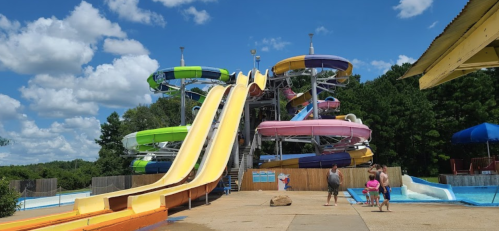 Colorful water slides at a water park under a blue sky, with families enjoying the area around the pool.