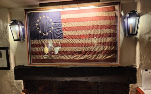 A vintage American flag with 13 stars displayed on a wall, flanked by two lanterns above a rustic fireplace.