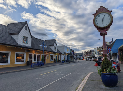 A quaint street lined with colorful shops and a vintage clock under a cloudy sky.