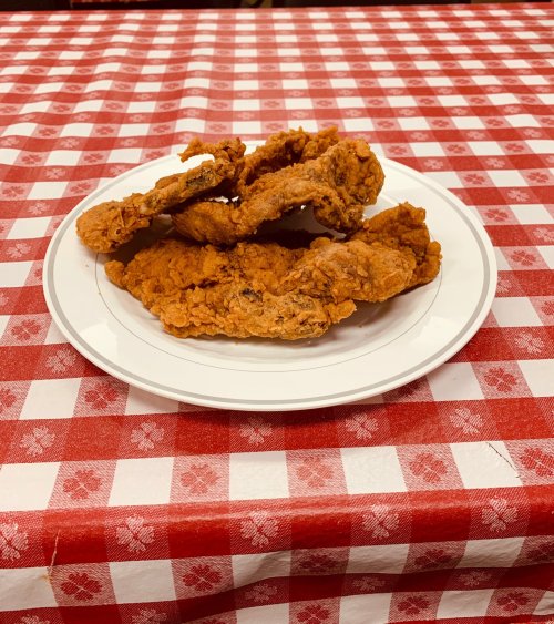 A plate of crispy fried chicken pieces on a red and white checkered tablecloth.