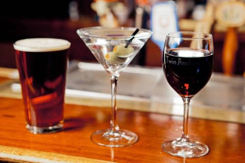 Three drinks on a bar: a pint of beer, a martini with an olive, and a glass of red wine.
