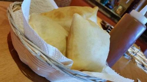 A basket of golden, crispy pastries with a bottle of sauce beside it, set on a wooden table.