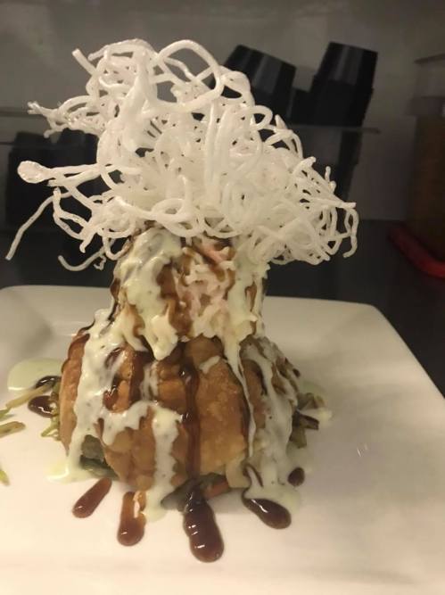 A plated dish featuring a crispy fried item topped with sauces and a decorative pile of crispy noodles.