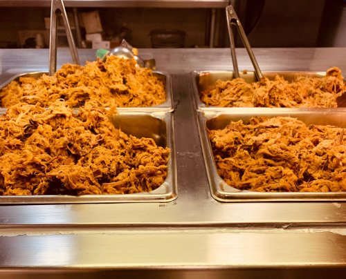 Two metal trays filled with shredded, cooked meat, displayed in a food service setting.