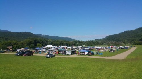 A vibrant outdoor market scene with tents and people set against a backdrop of green hills and a clear blue sky.