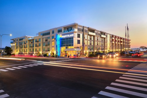 A modern hotel building at dusk, with illuminated signage and light trails from passing cars on the street.