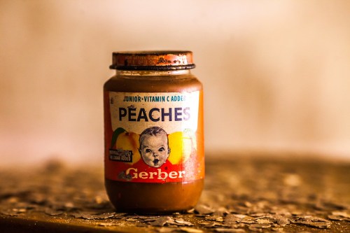 A vintage Gerber baby food jar labeled "Peaches," featuring a classic design and a baby photo on the label.