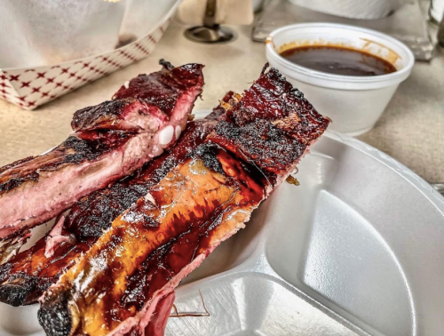 Close-up of smoked ribs on a plate, with a side of barbecue sauce in a cup.