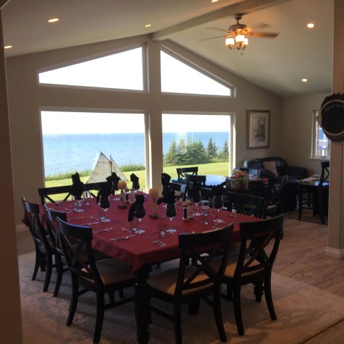 A dining room with a red tablecloth set for dinner, featuring large windows overlooking a scenic lake view.