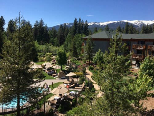 A scenic view of a resort with a pool, surrounded by trees and mountains under a clear blue sky.
