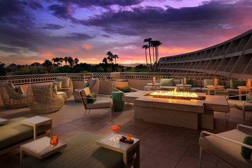 A stylish outdoor lounge with a fire pit, cozy seating, and a vibrant sunset sky in the background.
