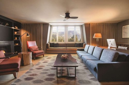 Modern living room with a large sofa, armchairs, a coffee table, and a window with shutters, featuring warm lighting.