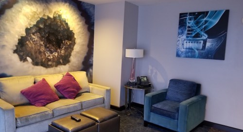 A modern living area featuring a sofa with purple pillows, a blue chair, and abstract wall art.
