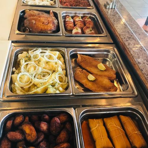 A buffet display featuring various dishes: roasted chicken, fish, potatoes with onions, plantains, and tamales.