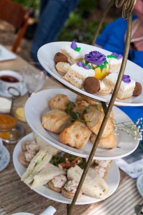 A tiered serving stand with assorted pastries, scones, and sandwiches, set in a garden setting.