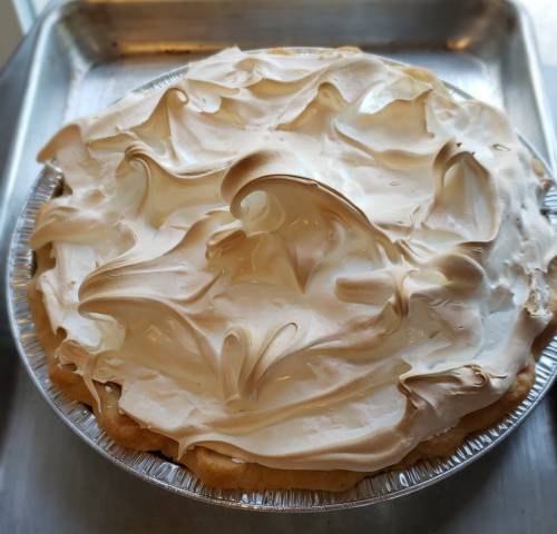 A freshly baked pie topped with swirls of golden meringue in a silver pie dish.