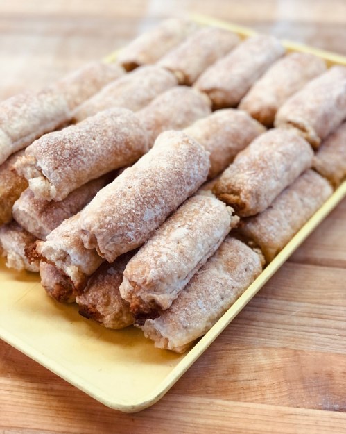 A yellow tray filled with neatly arranged, golden-brown rolled pastries on a wooden surface.