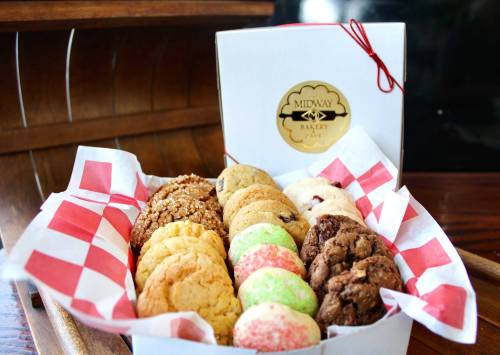 A box of assorted cookies, including chocolate chip, sugar, and festive green and red cookies, lined with checkered paper.
