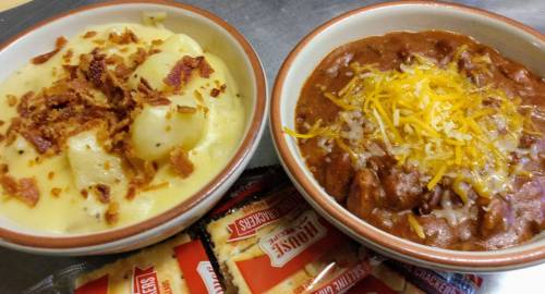 Two bowls of comfort food: one with creamy mashed potatoes topped with bacon, the other with chili and shredded cheese.