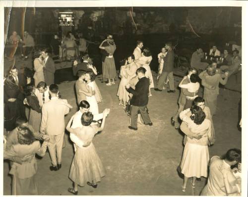 A vintage black-and-white photo of couples dancing in a lively social setting, with people enjoying the atmosphere.
