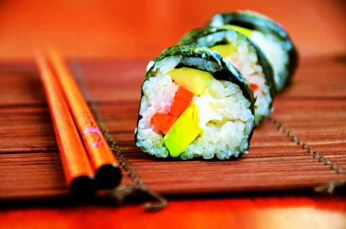 Three colorful sushi rolls on a bamboo mat, with chopsticks beside them.