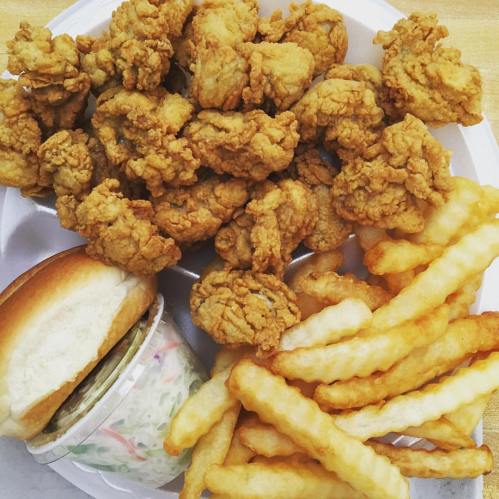 A plate of crispy fried chicken pieces, crinkle-cut fries, a sandwich, and a small cup of coleslaw.