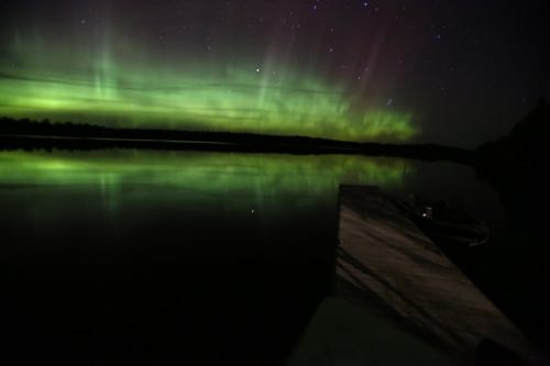 A serene lake reflecting vibrant green and purple auroras under a starry night sky.