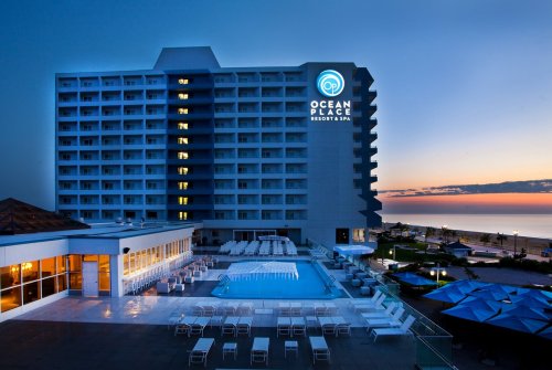 Ocean Place Resort & Spa at dusk, featuring a pool area and illuminated hotel sign against a colorful sky.