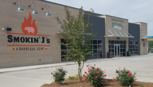 Exterior of Smokin' J's Barbeque Joint, featuring a modern building with a sign and landscaped flower beds.