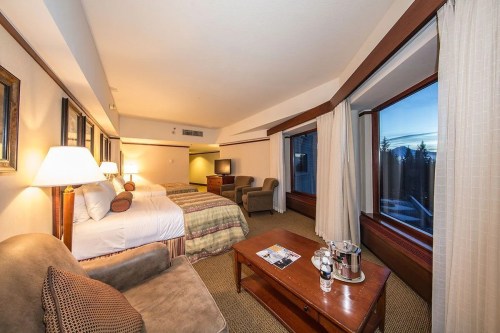 Cozy hotel room with two beds, a seating area, and large windows showcasing a scenic view.