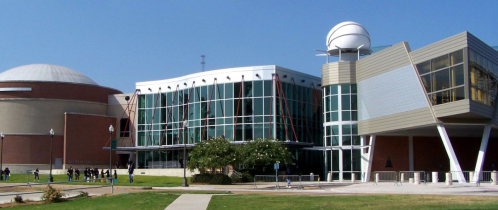 Modern building with large glass windows, a dome structure nearby, and a clear blue sky in the background.