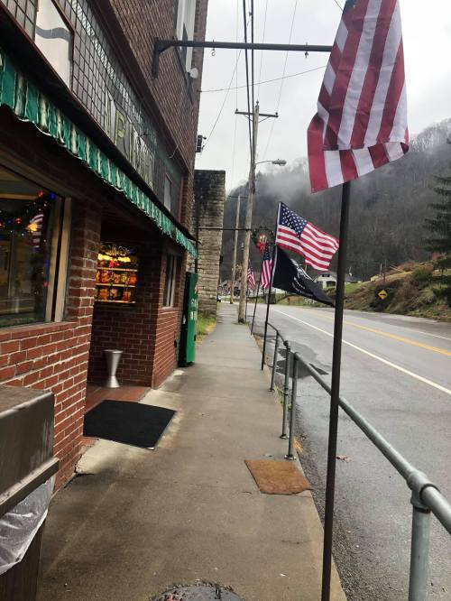 A rainy street scene featuring a brick building with flags and a sidewalk lined with American flags.