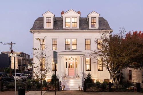 A large white house with multiple windows and a welcoming entrance, illuminated at dusk.