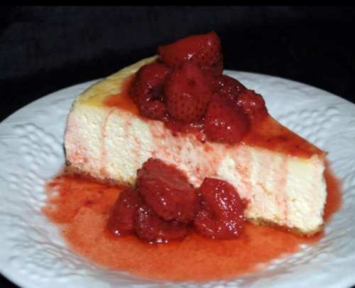 A slice of cheesecake topped with fresh strawberries and strawberry sauce on a decorative white plate.