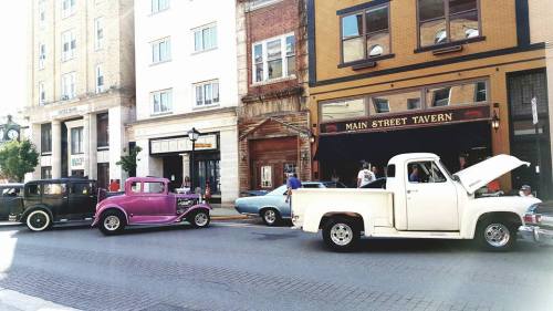 Classic cars parked on a street near Main Street Tavern, with people enjoying the sunny day.