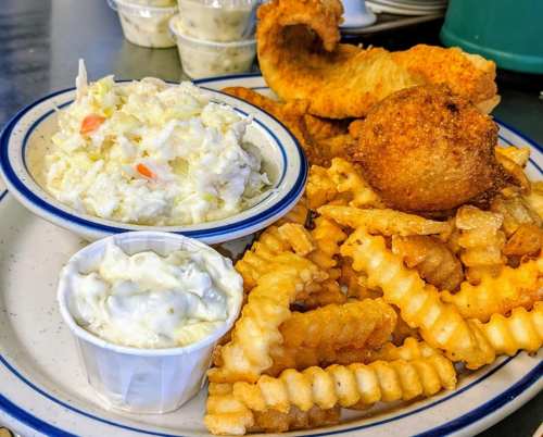 A plate of crispy fried fish, coleslaw, a hushpuppy, and crinkle-cut fries.