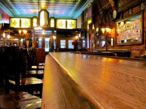 A cozy restaurant interior with wooden furniture, stained glass windows, and a man standing near the entrance.