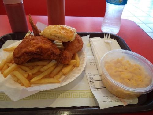 A tray with fried chicken, fries, a biscuit, and a side of macaroni, with condiments and a water bottle in the background.