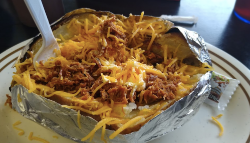 A loaded baked potato topped with shredded cheese and pulled meat, served on a plate with a plastic fork.