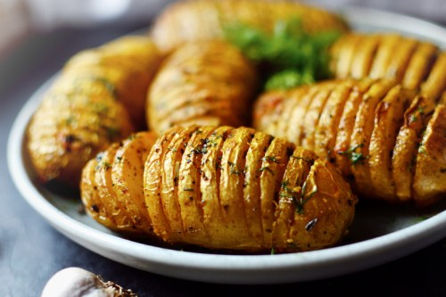 A plate of golden, crispy hasselback potatoes garnished with herbs, showcasing their sliced, fan-like appearance.
