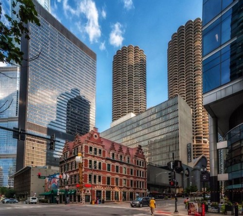 Historic building in foreground with modern skyscrapers behind, under a blue sky with scattered clouds.