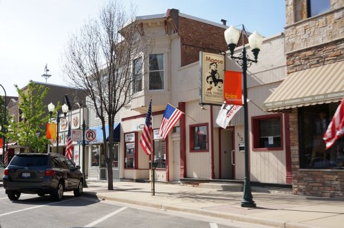 A charming street scene featuring shops with American flags, trees, and a clear blue sky.