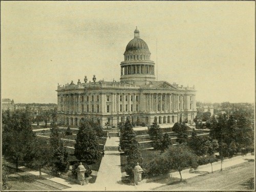 Historic building with a large dome, surrounded by trees and landscaped grounds, captured in a vintage style.