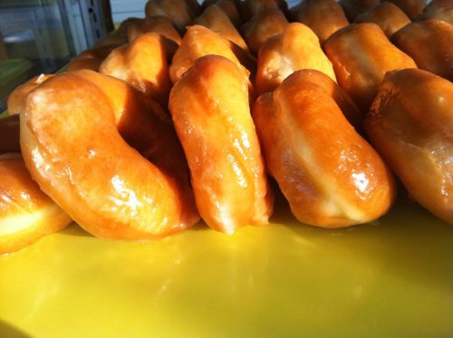 A close-up of glazed donuts arranged in a row on a yellow surface, showcasing their shiny, golden-brown exterior.